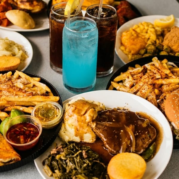 A table filled with various plates of Southern comfort food, including fried chicken, tacos, and drinks.