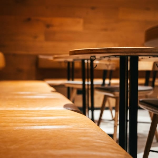 Warmly lit restaurant interior with a long leather booth and round wooden tables with stools.
