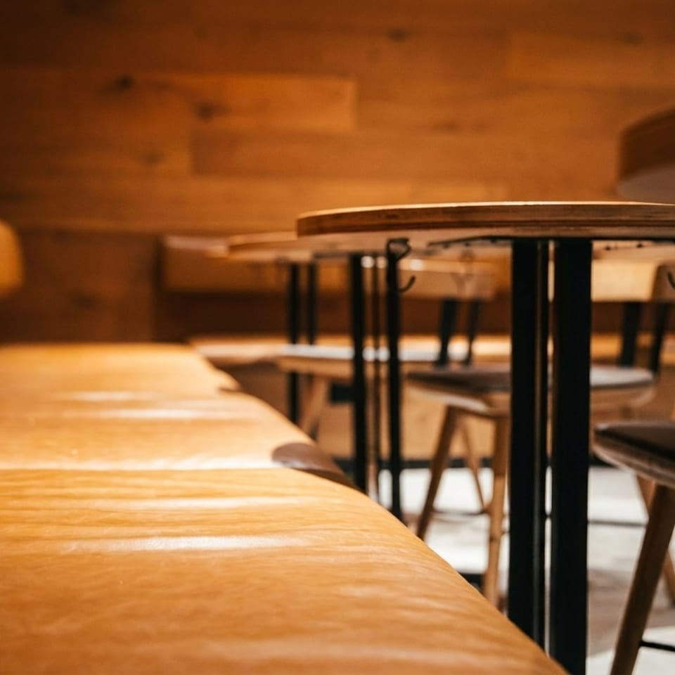 Warmly lit restaurant interior with a long leather booth and round wooden tables with stools.