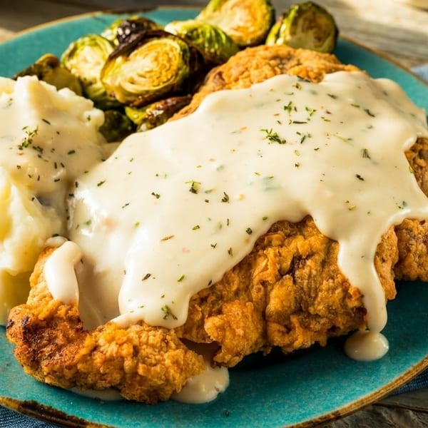 Country fried steak with gravy, mashed potatoes, and roasted Brussels sprouts on a teal plate.